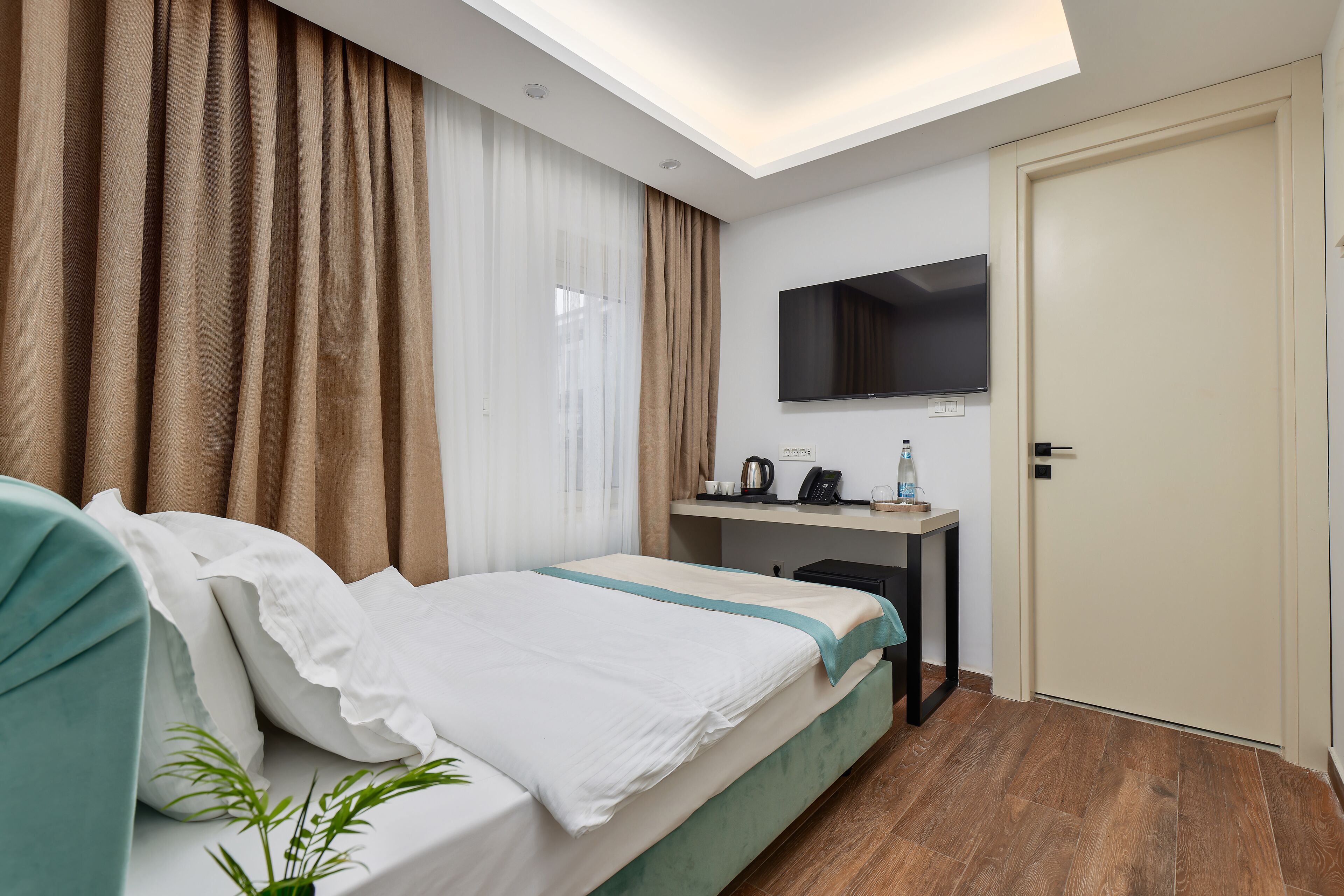 Habitación de hotel con una cama, un escritorio con televisor de pantalla plana, una puerta y una ventana con cortinas.