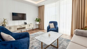Una sala de estar moderna con un televisor de pantalla plana, un sillón azul, un sofá color beige y una mesa de centro de mármol.