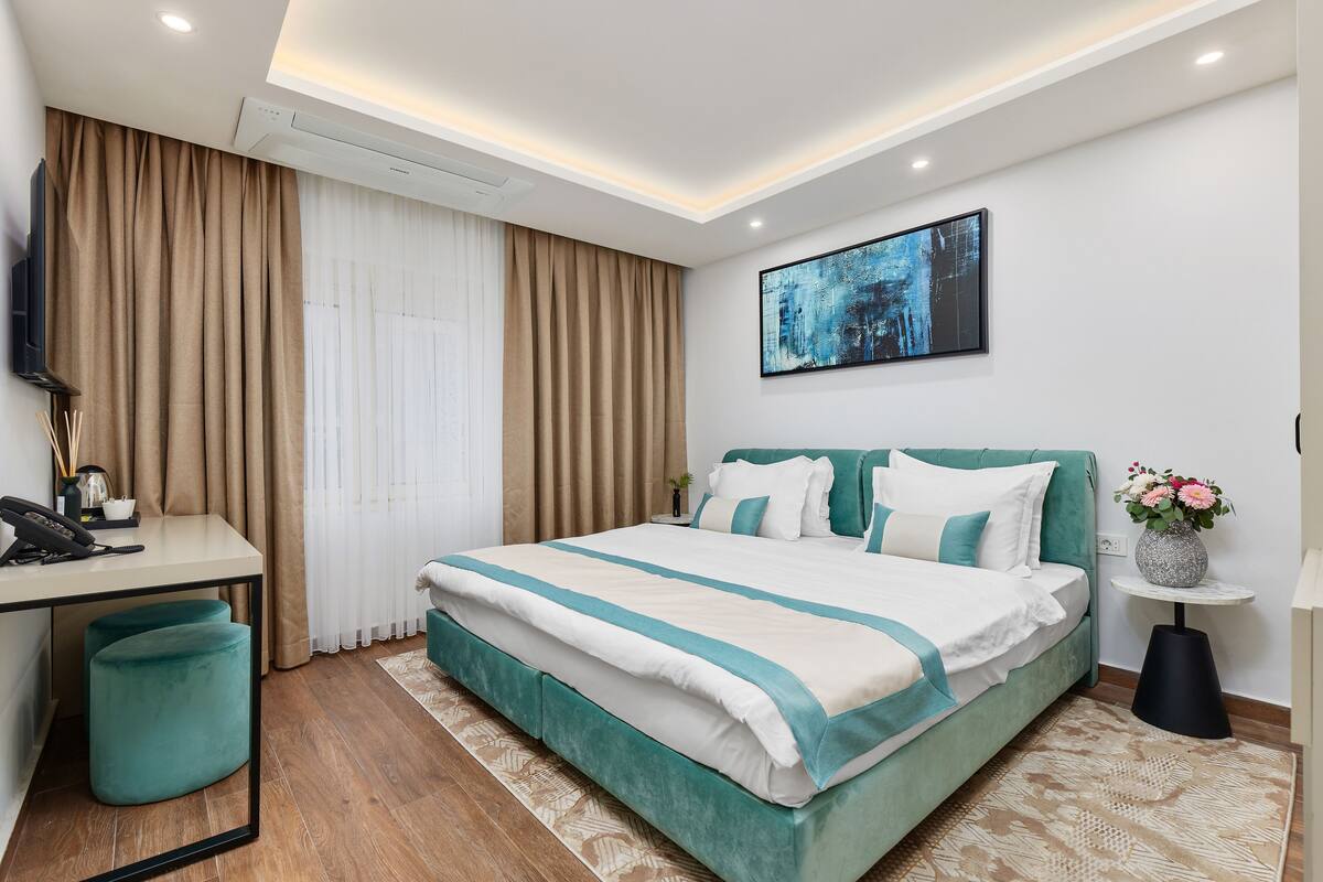 A modern hotel room with a bed, desk, and a painting on the wall.