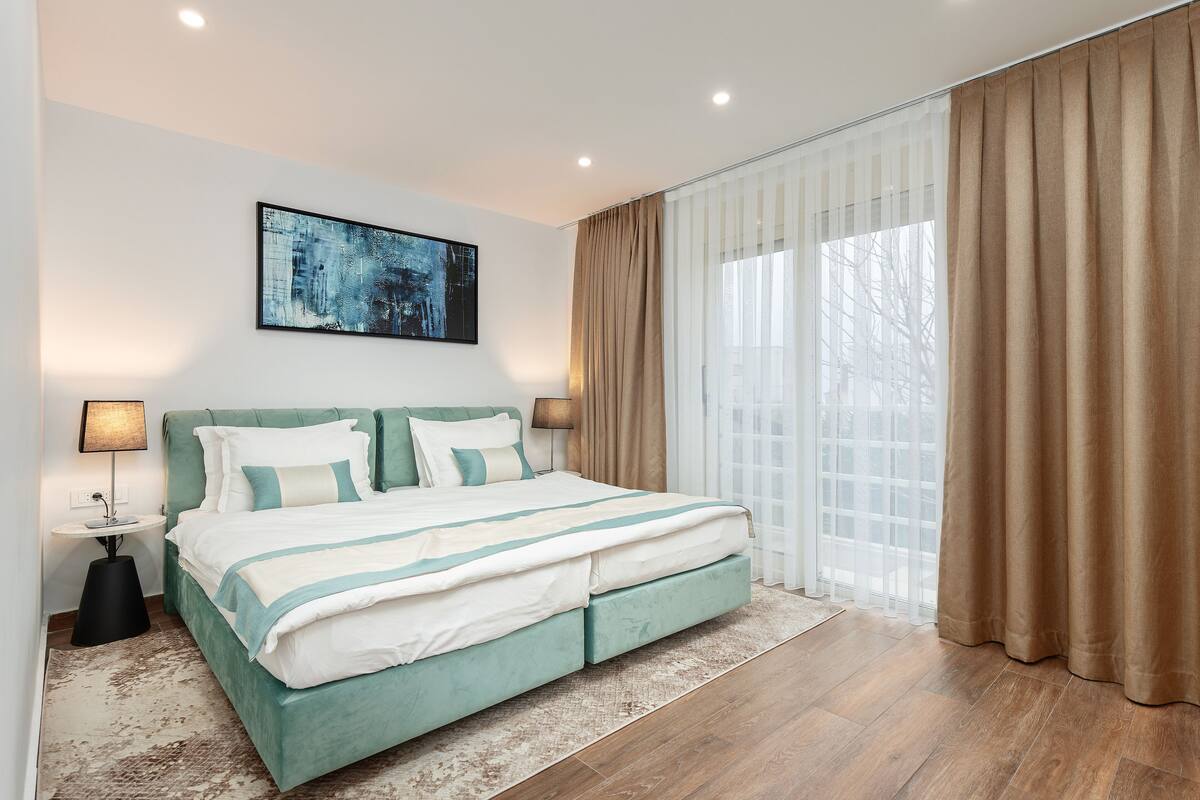 A modern bedroom with a large bed, a nightstand, a lamp, and a window with curtains.