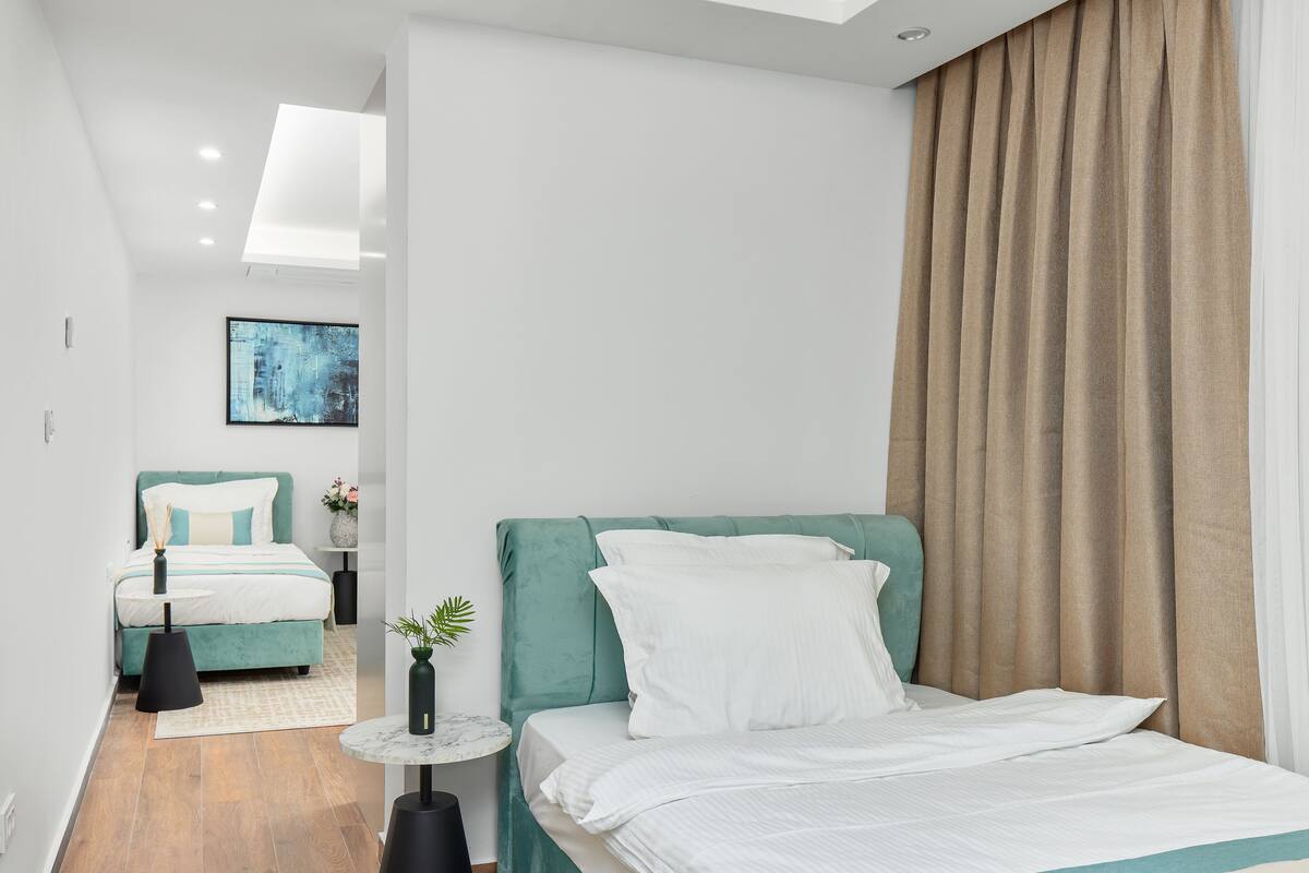 A modern hotel room with a large bed, a smaller bed, a round table, and a potted plant.