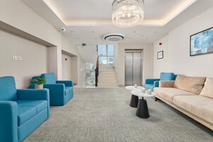 A modern lobby with blue and beige sofas, a marble coffee table, and a chandelier.