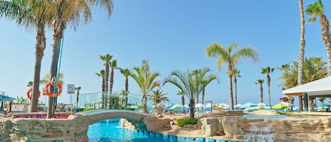 A pool area with palm trees, a bridge, and a clear blue sky.