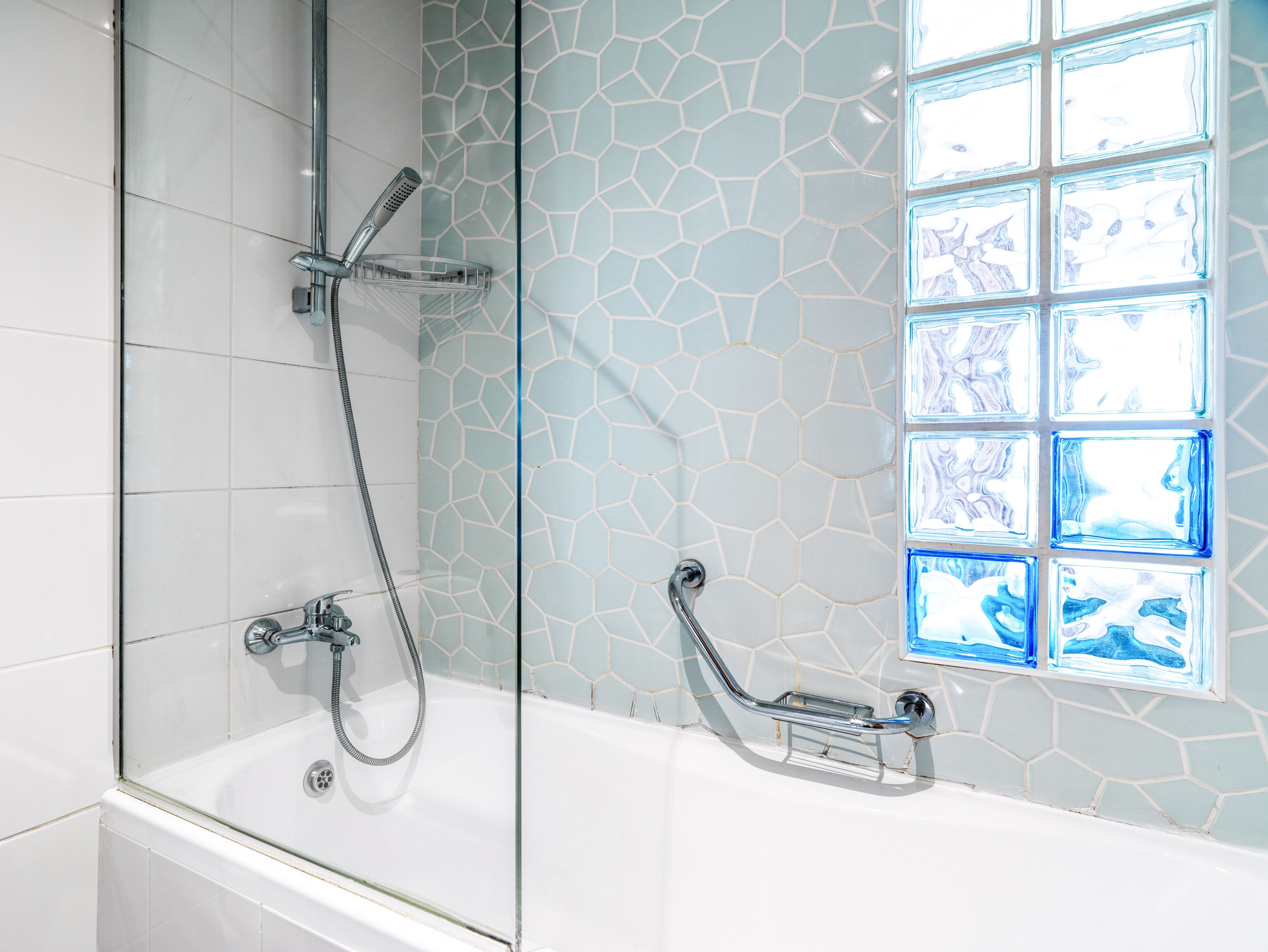 A glass-enclosed shower with a modern design, a white bathtub, and a mosaic tile wall.