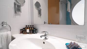 A bathroom with a white sink, two round mirrors, a towel rack, and a shelf with various toiletries.
