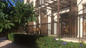 A building with a covered outdoor area, a paved walkway, and a garden with various plants and flowers. - Hotel Kings Annex (Paphos)