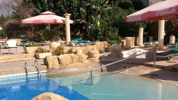 A pool area with a Coca-Cola branded umbrella, lounge chairs, and a stone wall. - Hotel Kings Annex (Paphos)
