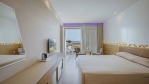 A hotel room with a bed, a desk with a coffee maker, a TV, and a view of the beach. - Tasia Maris Seasons (Ayia Napa)