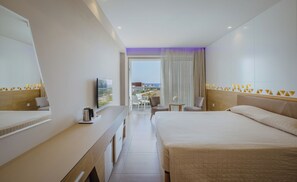A hotel room with a bed, a desk with a coffee maker, a TV, and a view of the beach. - Tasia Maris Seasons (Ayia Napa)