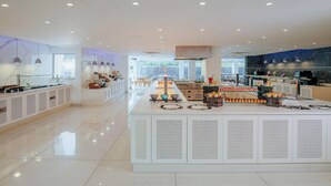 A modern, spacious cafe with a central counter displaying pastries and a seating area with tables and chairs. - Tasia Maris Seasons (Ayia Napa)
