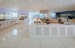 A modern, spacious cafe with a central counter displaying pastries and a seating area with tables and chairs. - Tasia Maris Seasons (Ayia Napa)