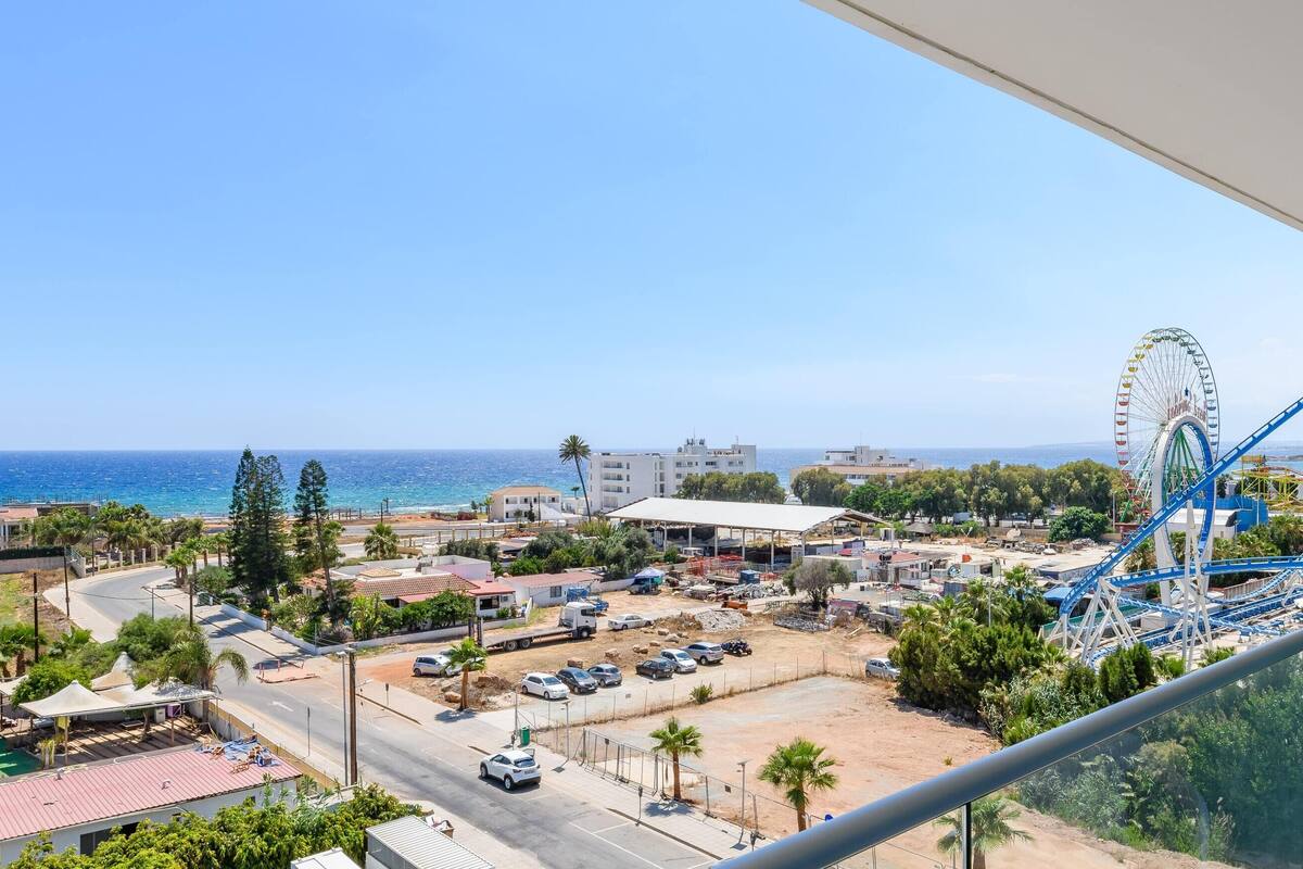 A coastal view from a balcony overlooking a beach, a parking lot, and a roller coaster.