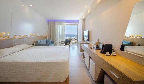 A modern hotel room with a large bed, a desk with a coffee machine, and a view of the sea. - Tasia Maris Seasons (Ayia Napa)