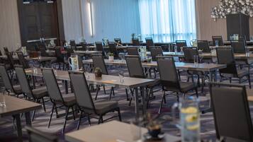 Un salón de conferencias con varias mesas y sillas dispuestas en filas, con jarras de agua y pequeñas plantas en cada mesa.