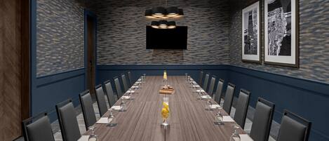A conference room with a long table, chairs, a TV screen, and framed artwork on the wall.