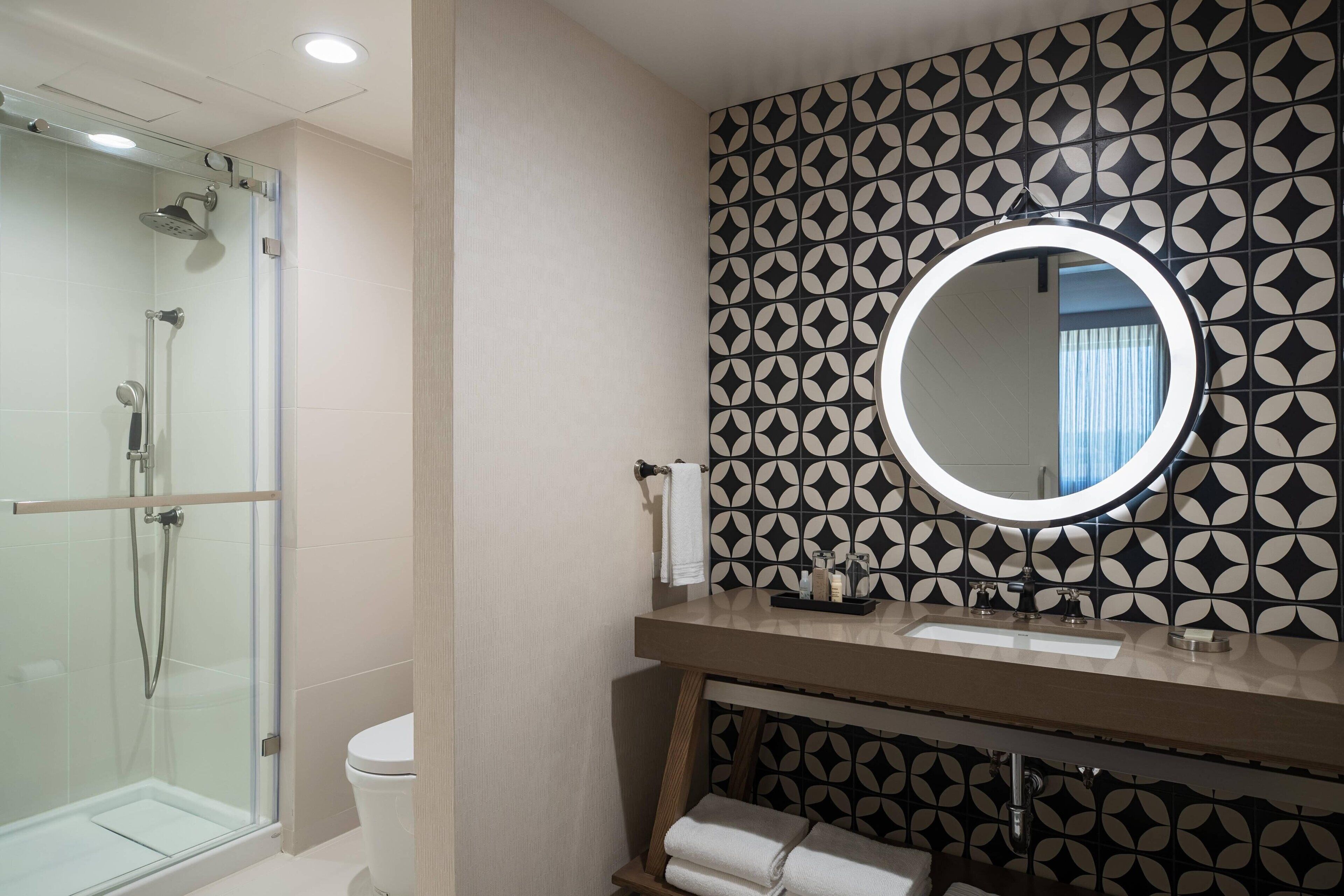 Un baño con ducha acristalada, lavabo con espejo y azulejos con diseño.