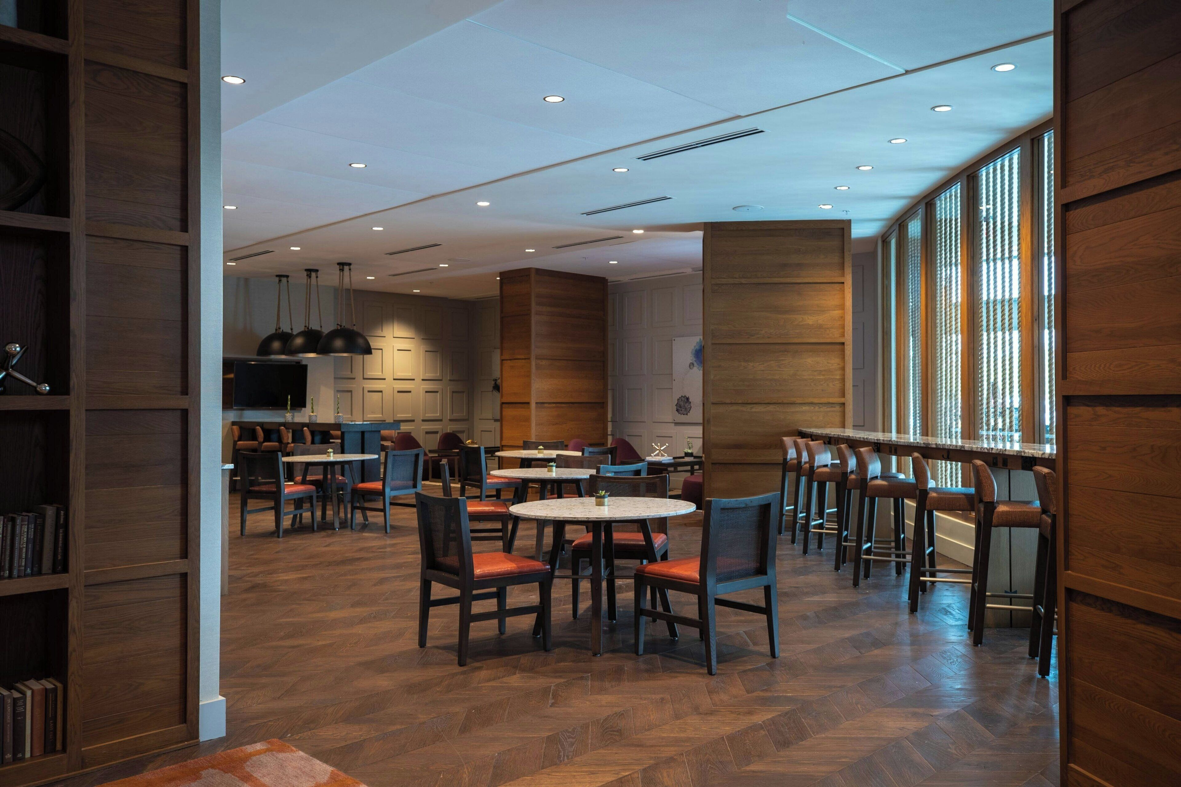 A modern restaurant with wooden paneling, round tables, and bar stools.