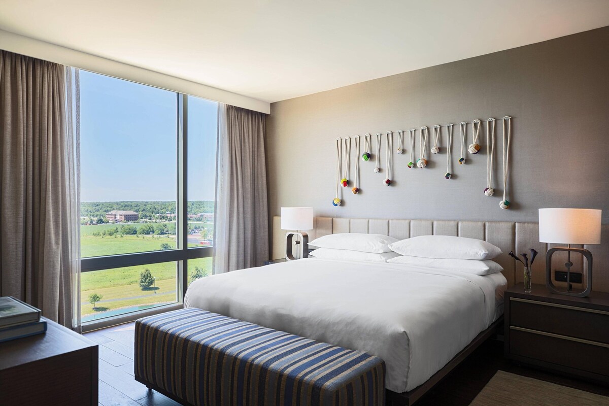 A hotel room with a large bed, a bench, a nightstand, and a view of the outdoors.