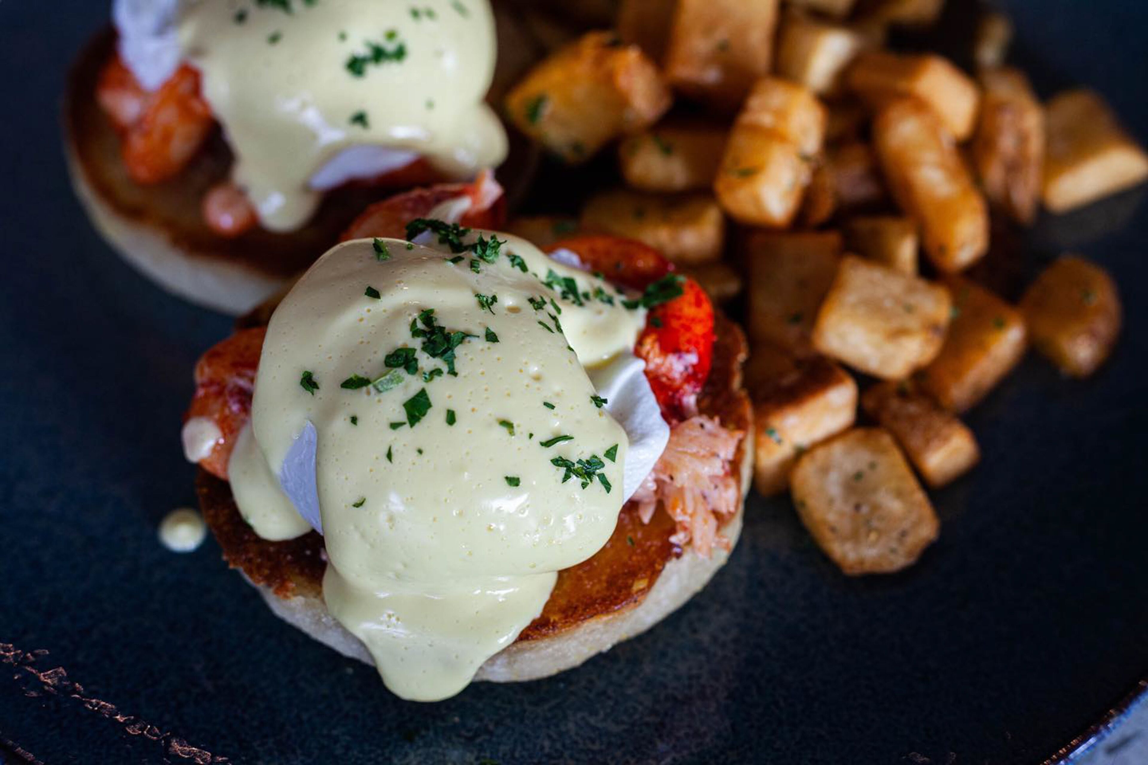 Prato de café da manhã com ovos benedict, molho holandês e batatas tostadas.
