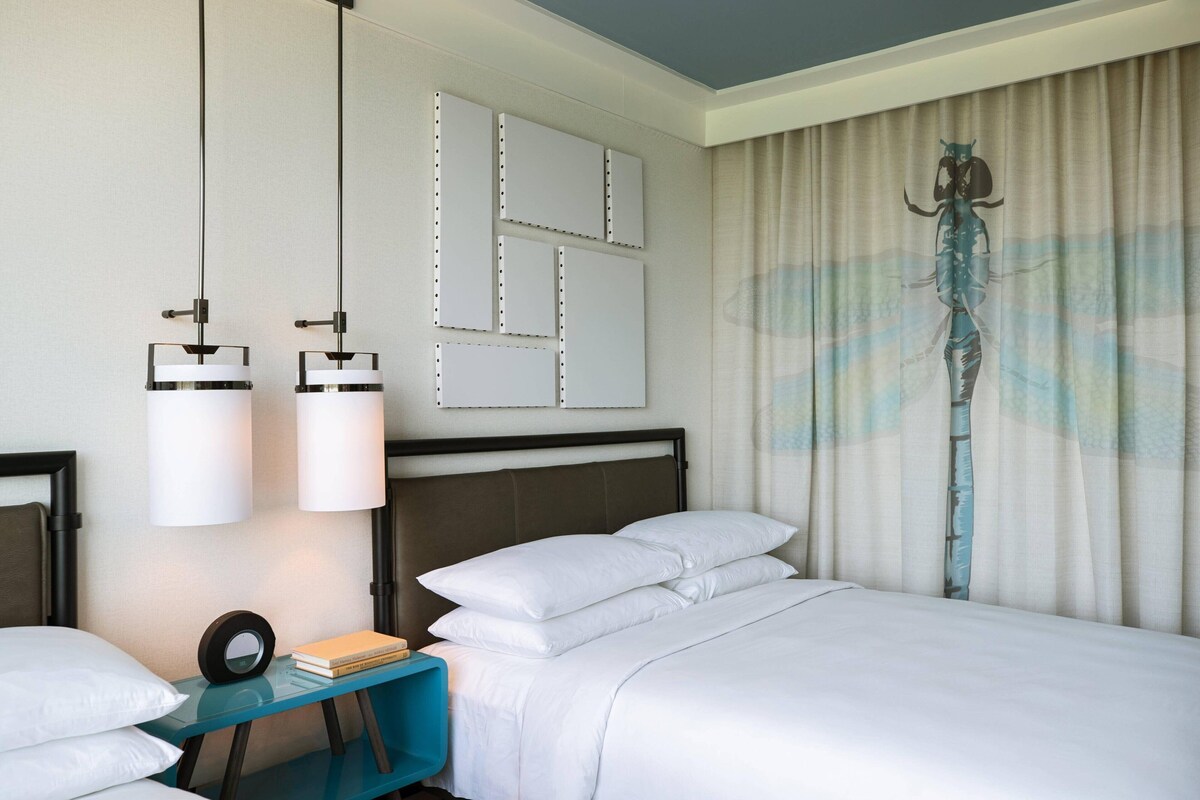 A hotel room with a bed, two bedside tables, a mirror, and a curtain with a sea creature design.