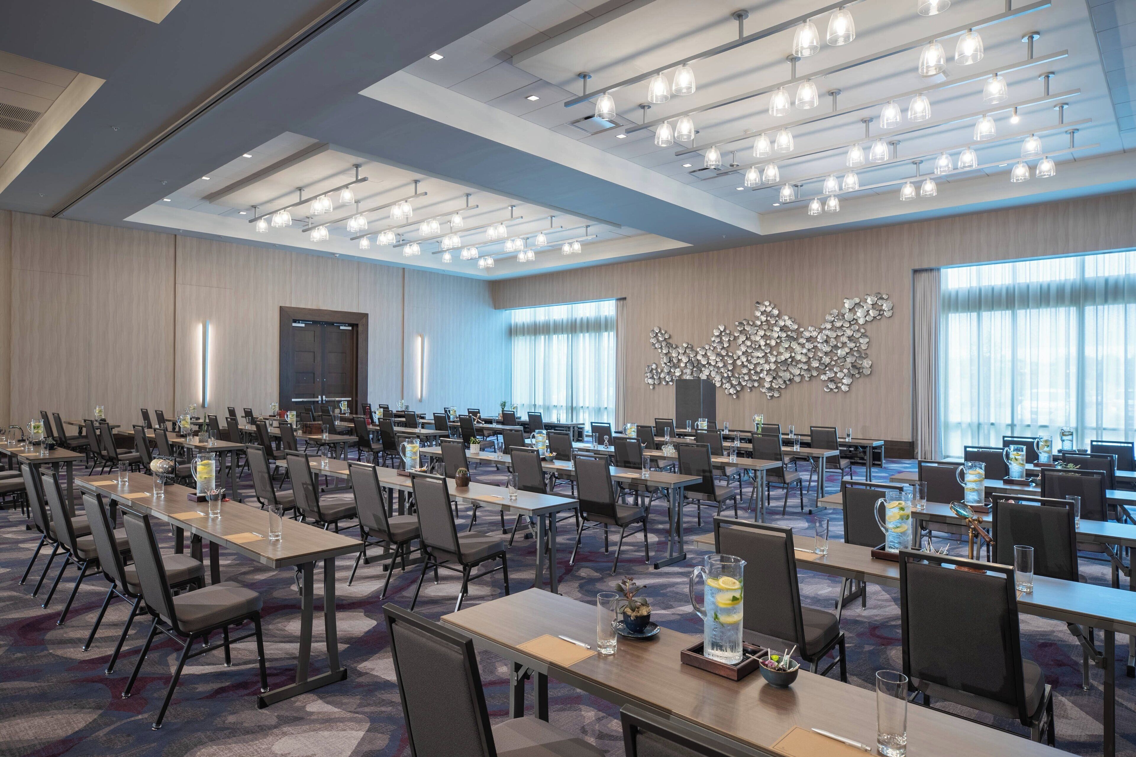 A large conference room with multiple tables and chairs, ceiling lights, and a decorative wall piece.