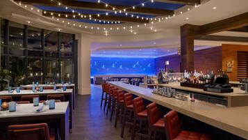 A modern bar area with a long counter, red bar stools, and a bar stocked with bottles.