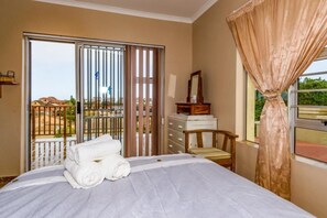 A hotel room with a bed, a wooden chair, a dresser, and a balcony with a view of the outside.