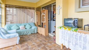 A living room with a sofa, a coffee table, a television, and a kitchen area with a microwave. - Tuscany On Sea (Great Brak River)