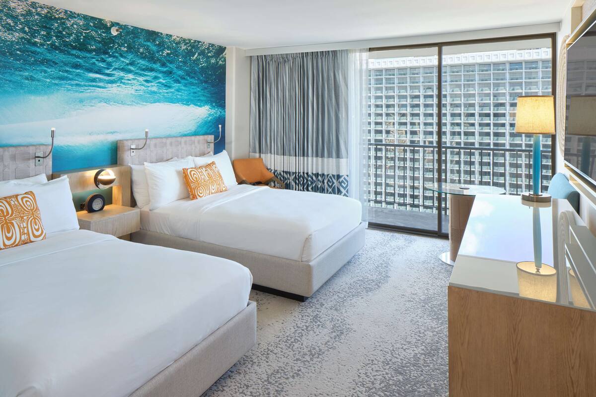 A hotel room with two beds, a large window with curtains, a view of a cityscape, and a nightstand with a lamp.