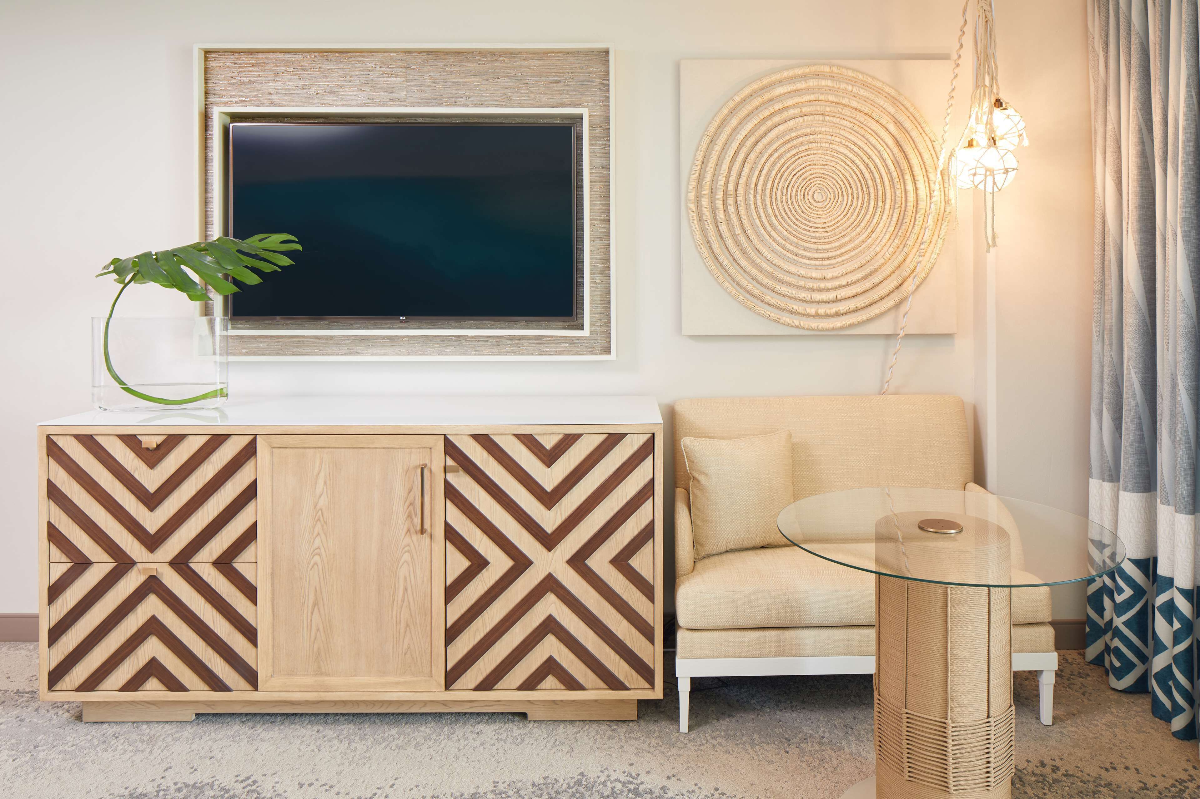 A living room with a modern TV, a decorative wall hanging, and a glass coffee table.