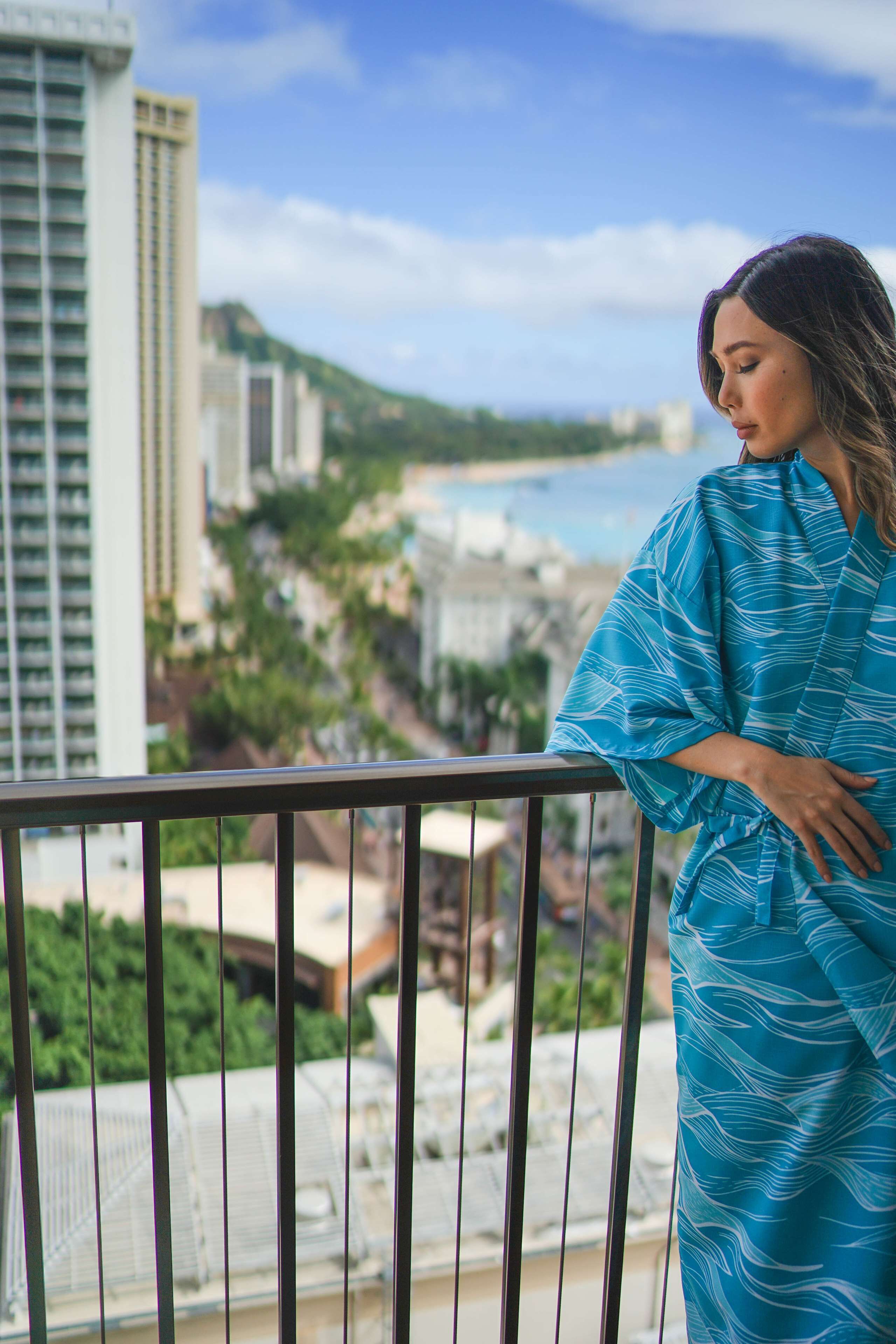 A person standing on a balcony overlooking a cityscape with buildings and a beach.