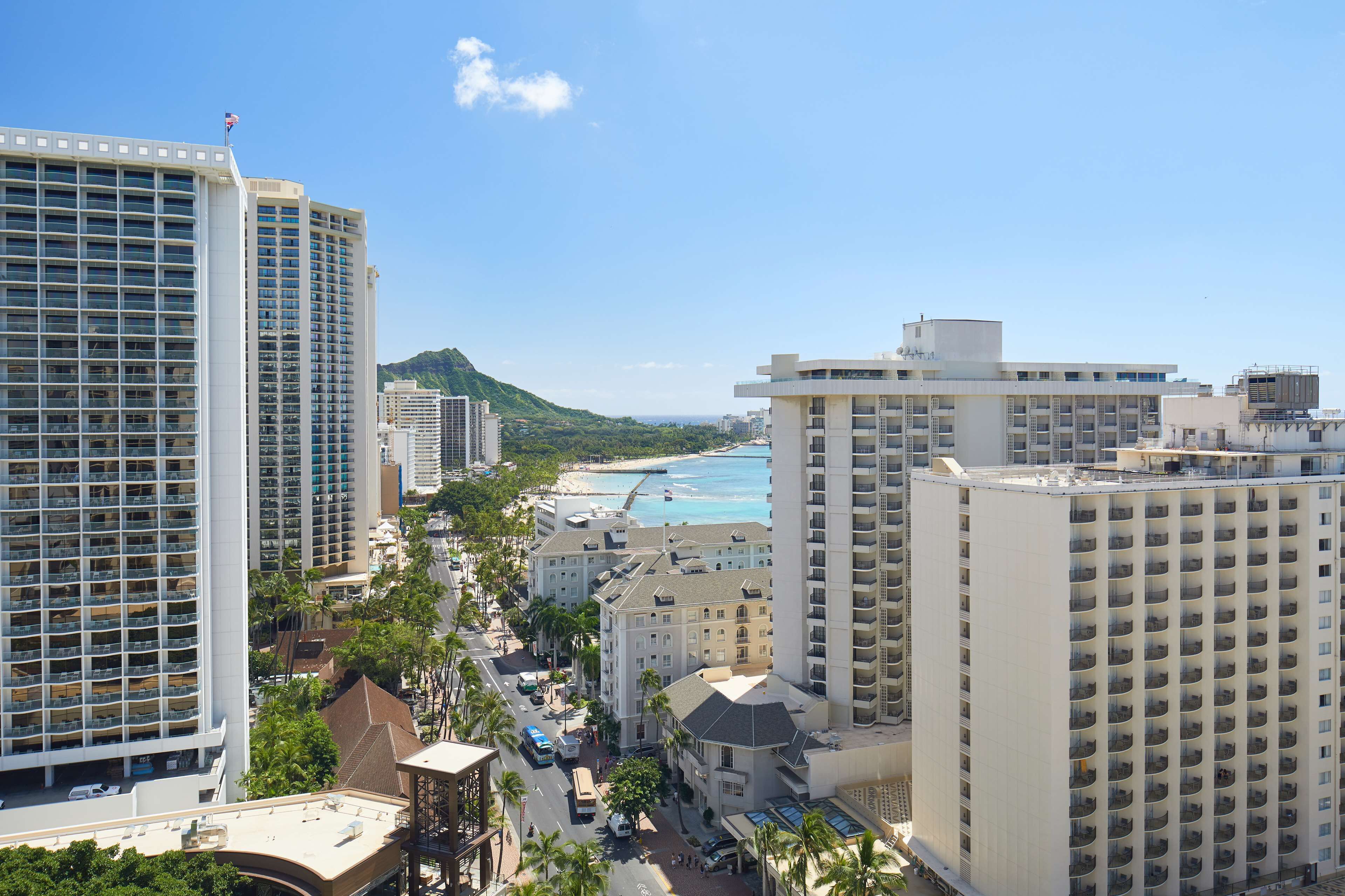 A high-rise hotel with multiple floors, a beach view, and a mountainous backdrop.