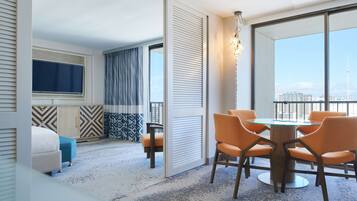 Une chambre d’hôtel avec une grande fenêtre, un coin repas avec des chaises orange, un lit et un téléviseur.
