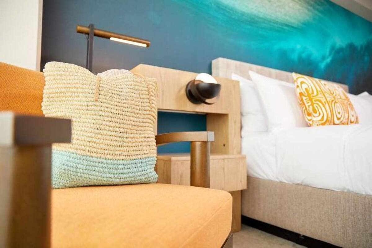 A modern hotel room with a bed, a nightstand, a lamp, and a wall painting.