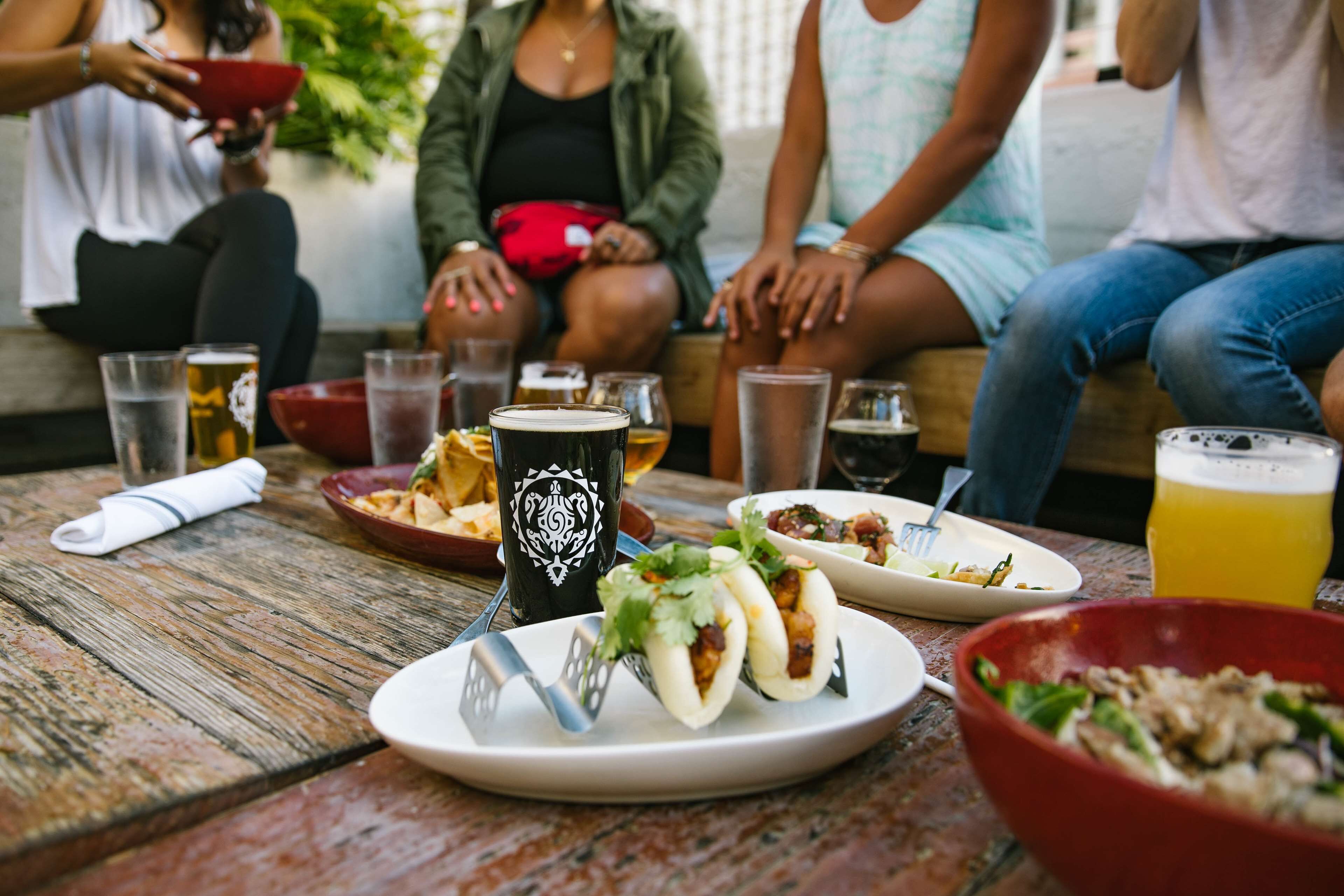 A group of people sitting at a wooden table with food and drinks.