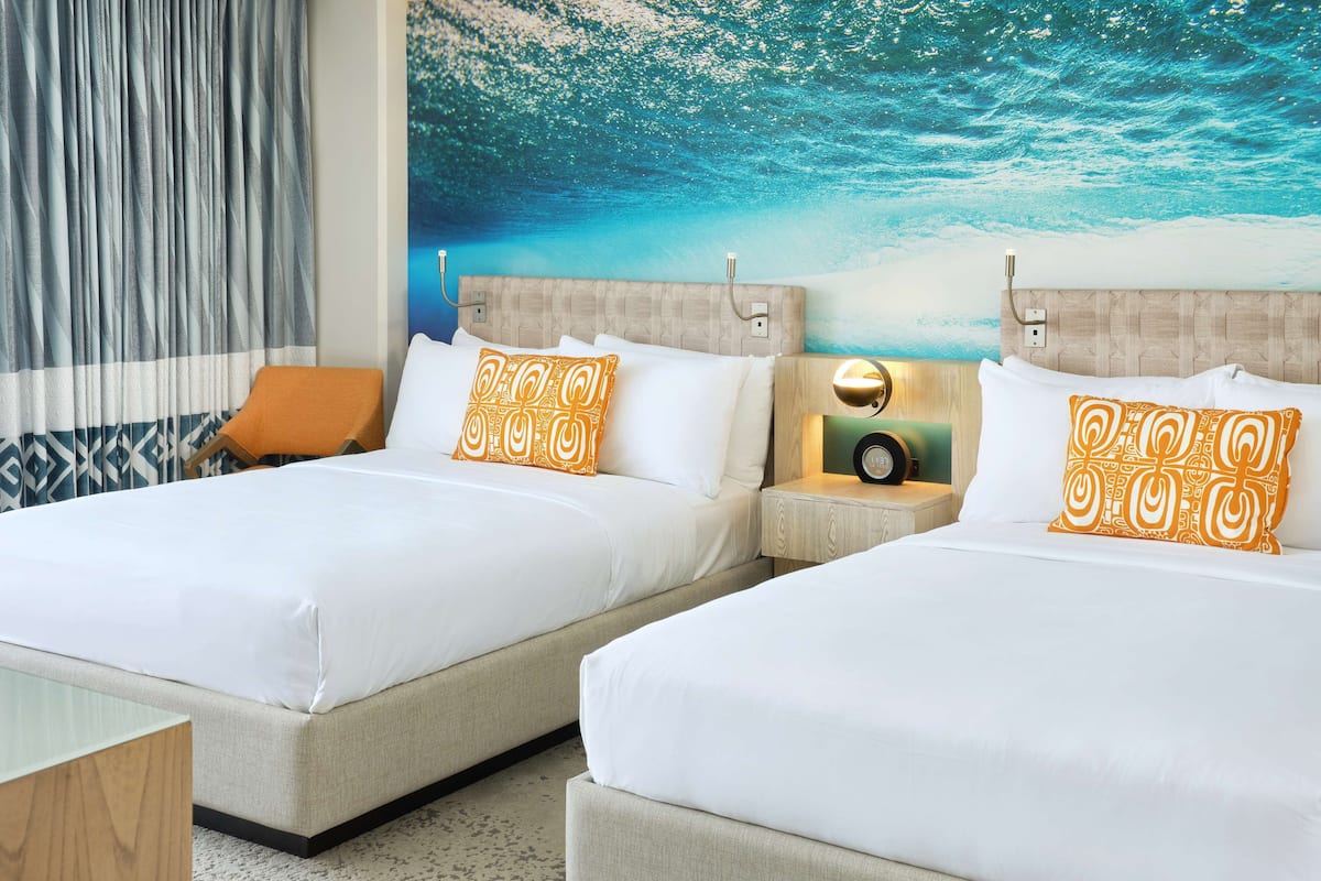 A hotel room with two beds, a wooden headboard, a wall mural, and a bedside table with a clock.