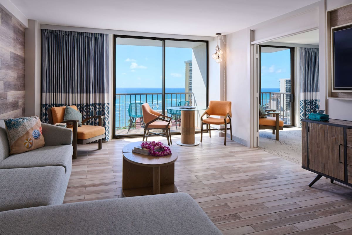 A spacious living area with a balcony overlooking the sea, furnished with a sofa, chairs, and a coffee table.