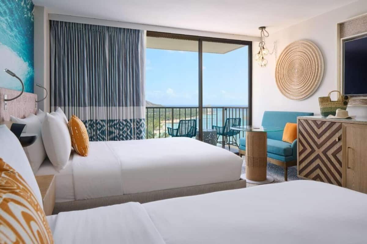 A hotel room with two beds, a balcony with a view, a sofa, and a TV.