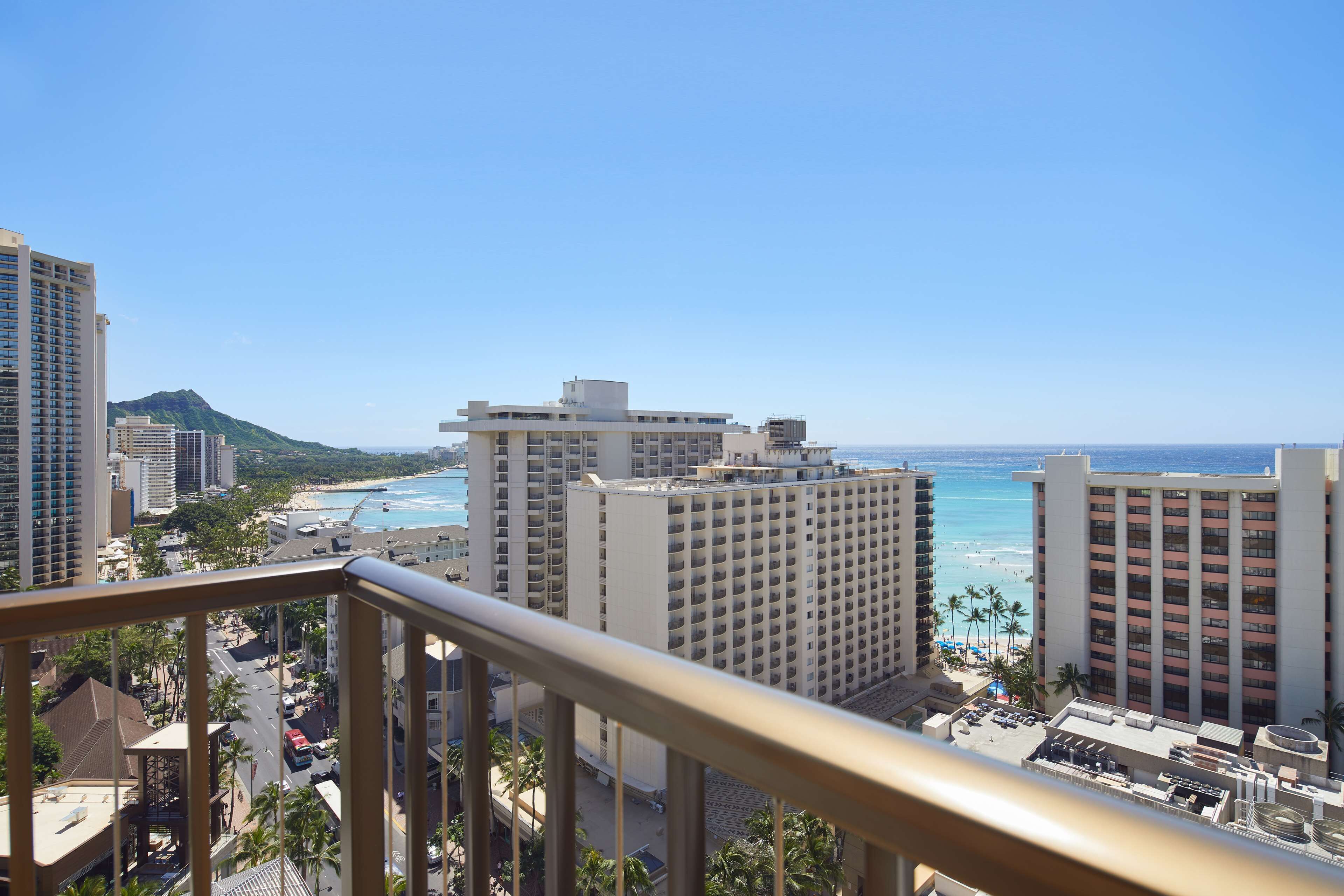A high-rise hotel overlooking a beach with clear blue waters and a mountain in the background.