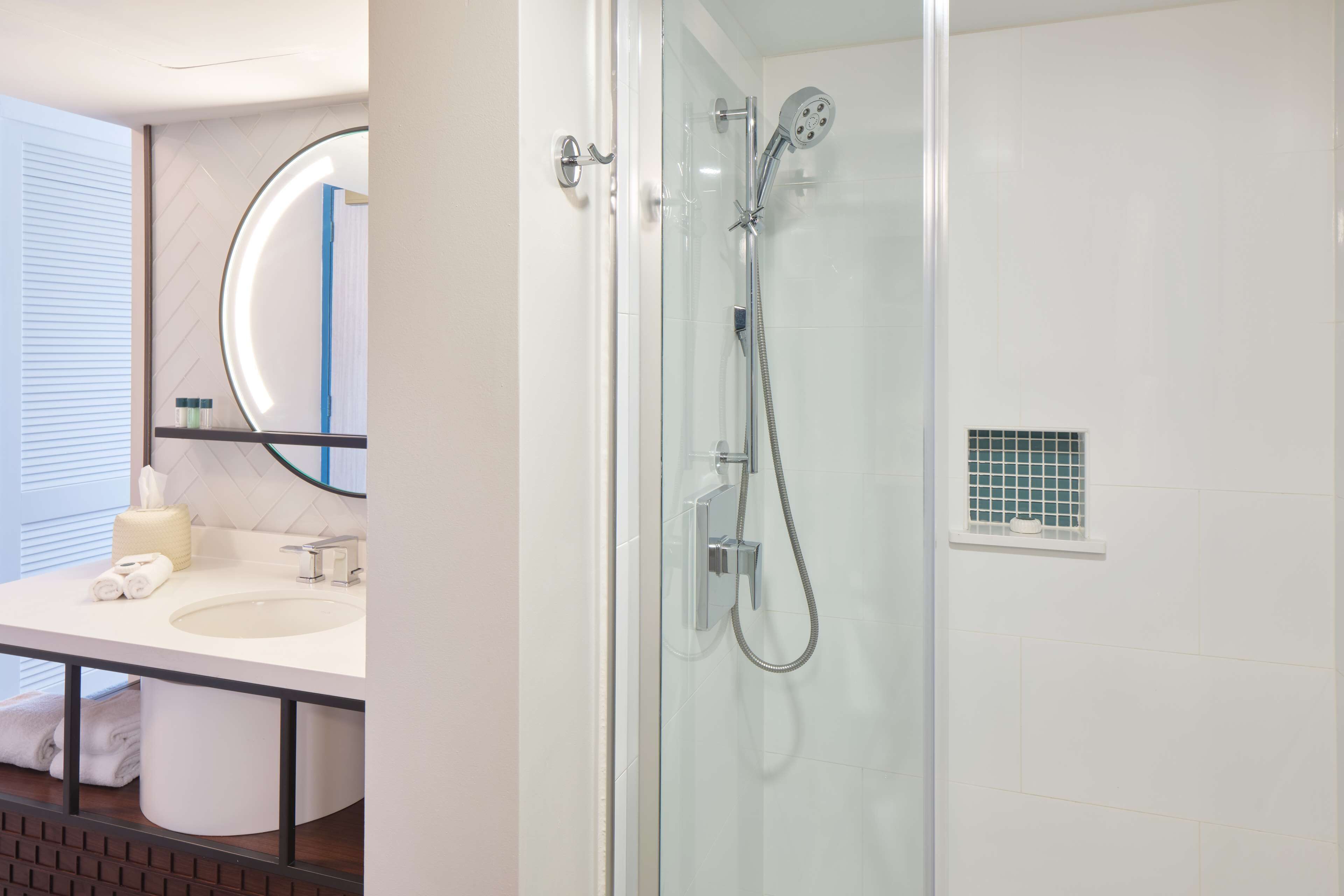 Un baño moderno con ducha acristalada, lavamanos con espejo y pequeña ventana de celosía.