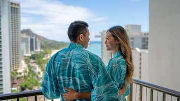 A couple standing on a balcony overlooking a cityscape with buildings and a distant mountain.