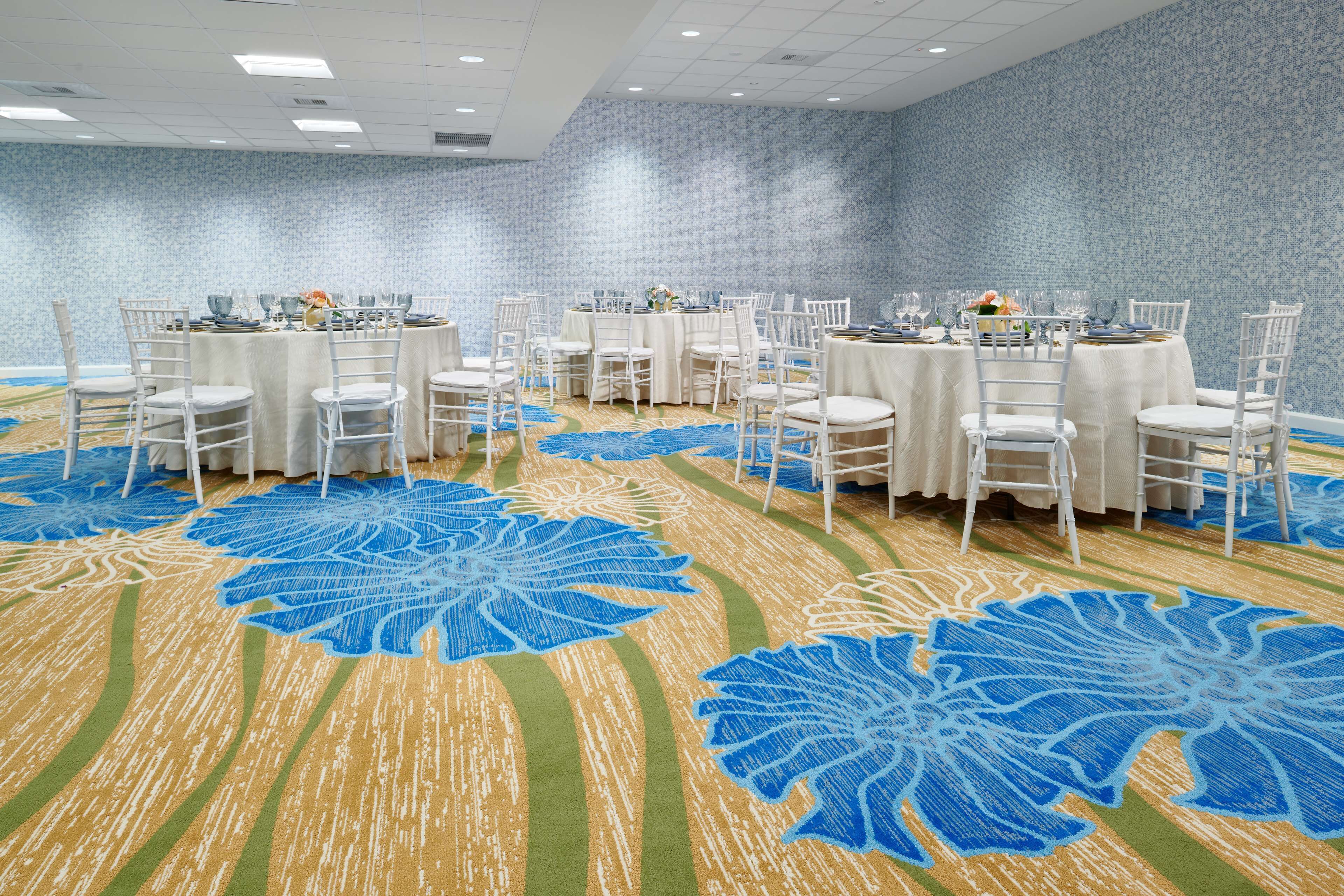 A conference room with round tables, white chairs, and a blue floral carpet.