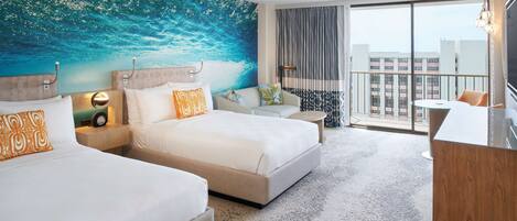 A hotel room with two beds, a desk, a chair, a large window with a view of buildings, and a wall mural.