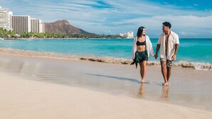 Una pareja caminando por la playa con un paisaje urbano al fondo.