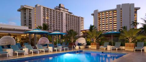 A hotel pool area with lounge chairs and umbrellas, surrounded by tall buildings.
