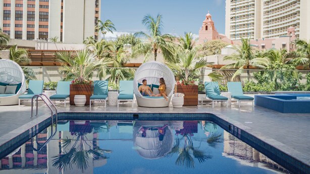 Un área de piscina con sillones de descanso, un jacuzzi y palmeras.