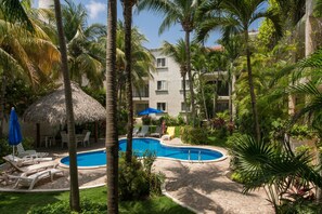 A pool area with lounge chairs, a thatched umbrella, and palm trees.