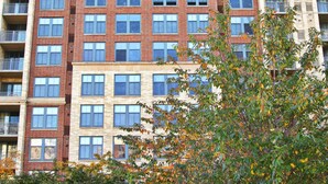 A high-rise residential building with multiple balconies, a central entrance, and surrounding greenery. - Weichert Suites at Arlington Courthouse (Arlington)