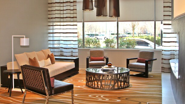 A modern hotel lobby with a sofa, chairs, a coffee table, and large windows offering a view of the street. - Weichert Suites at Arlington Courthouse (Arlington)