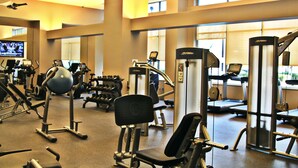 A gym with various exercise equipment, a television, and large windows allowing natural light. - Weichert Suites at Arlington Courthouse (Arlington)